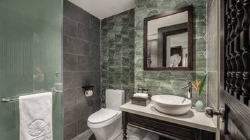 Un baño moderno con cabina de ducha de vidrio, inodoro, lavabo con espejo y tocador de madera oscura.