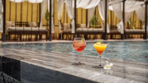 A poolside area with two drinks on a marble surface, a canopy structure, and a seating area in the background. - The Signature Hoi An (Da Nang)