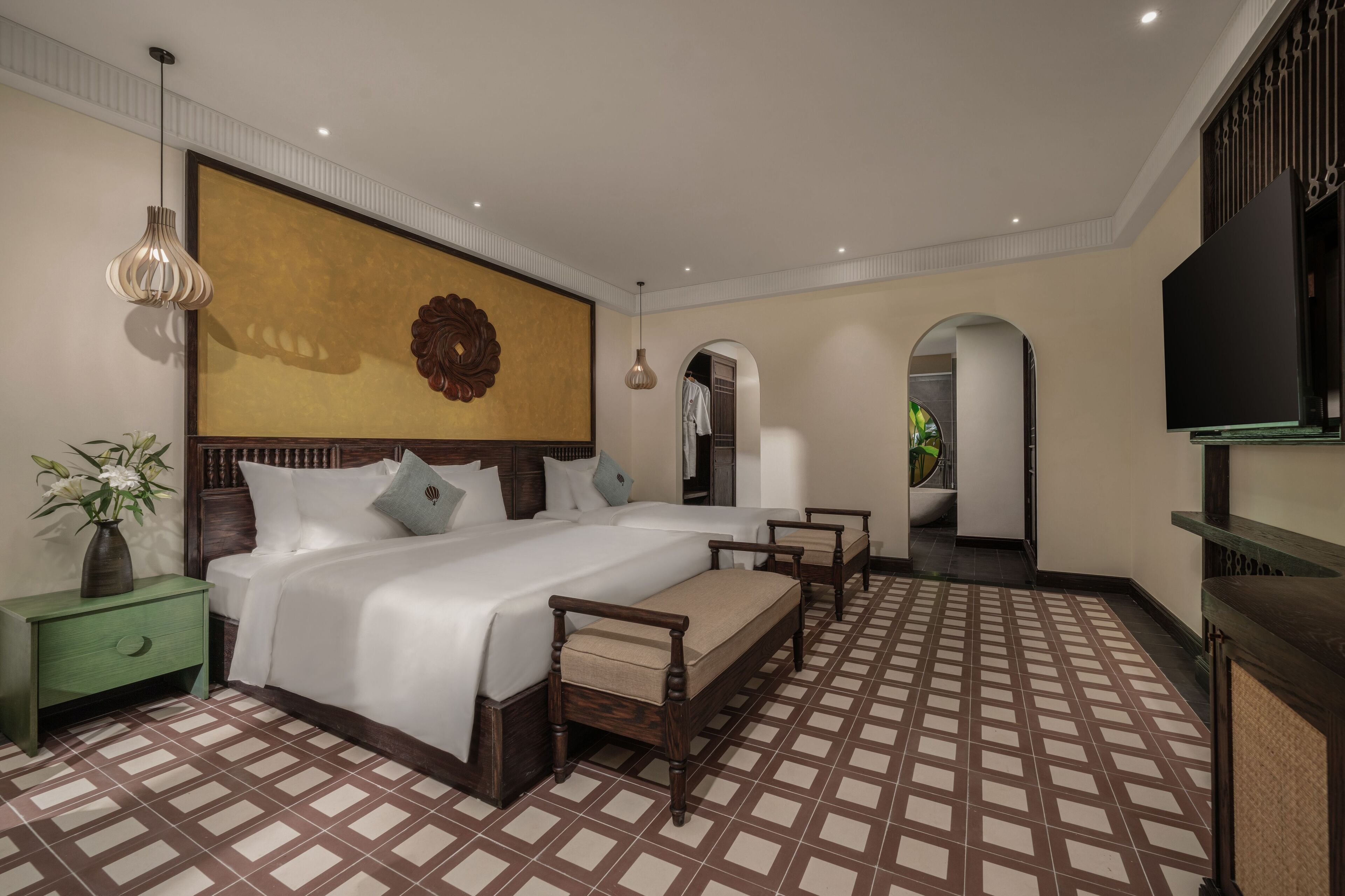 A hotel room with a large bed, a wooden headboard, a green nightstand, a decorative wall piece, and a television.