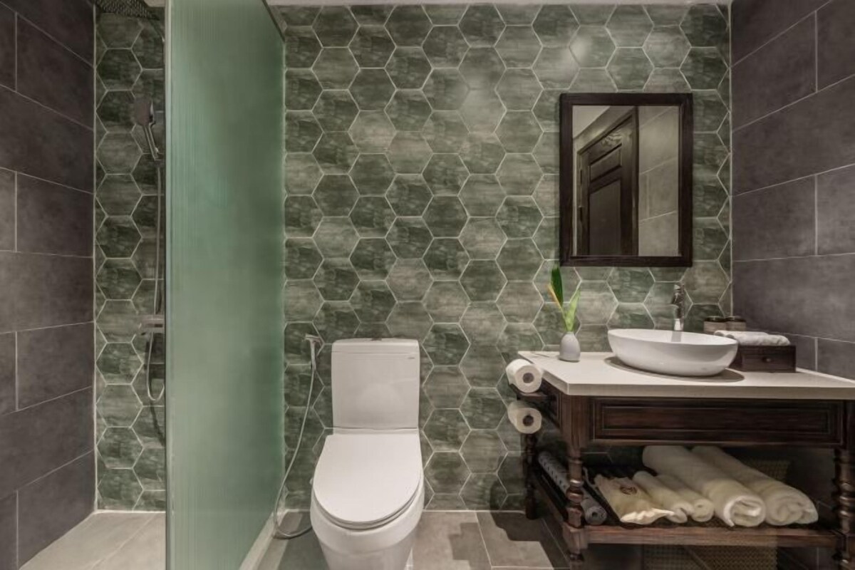 Un baño con salpicadero de azulejos hexagonales, un inodoro, un lavabo con espejo y un perchero con toallas.