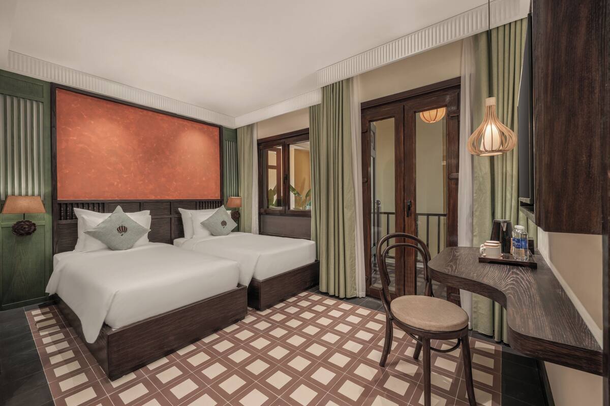 Ein Hotelzimmer mit zwei Betten, einem Schreibtisch, einem Stuhl und einem großen Spiegel.