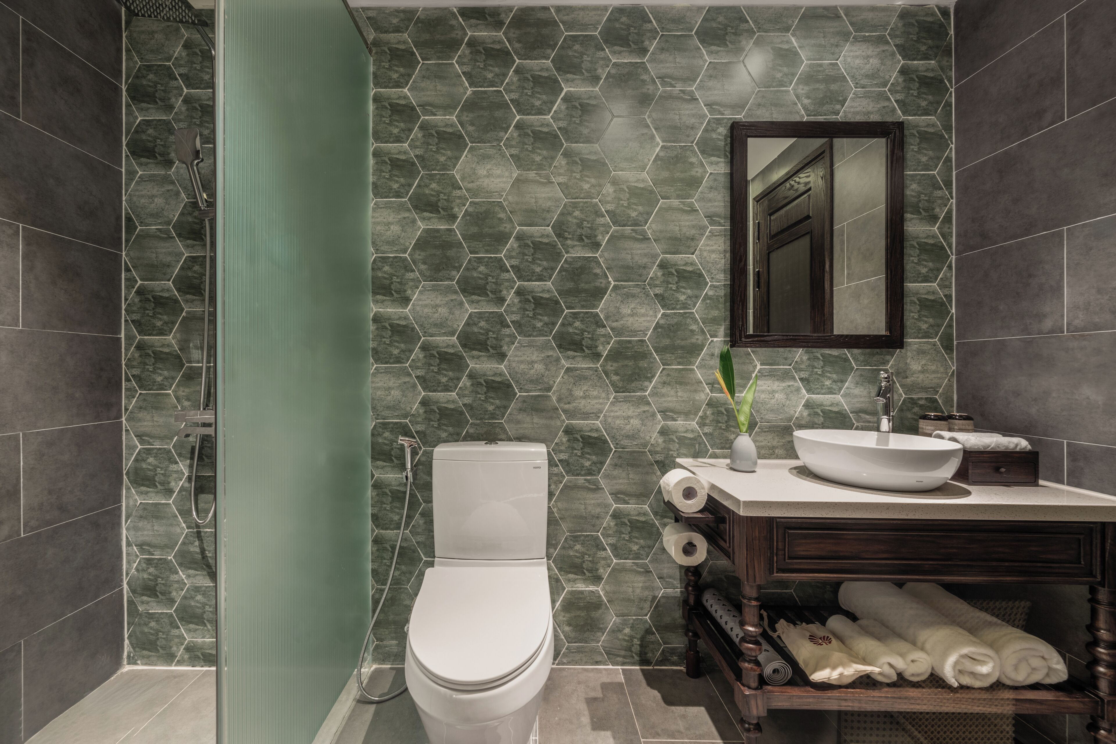 A bathroom with a hexagonal tile backsplash, a white toilet, a sink with a mirror above it, and a towel rack with towels.