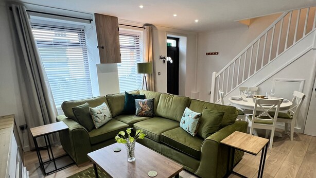A modern living room with a green sofa, a wooden coffee table, and a staircase leading to another level.