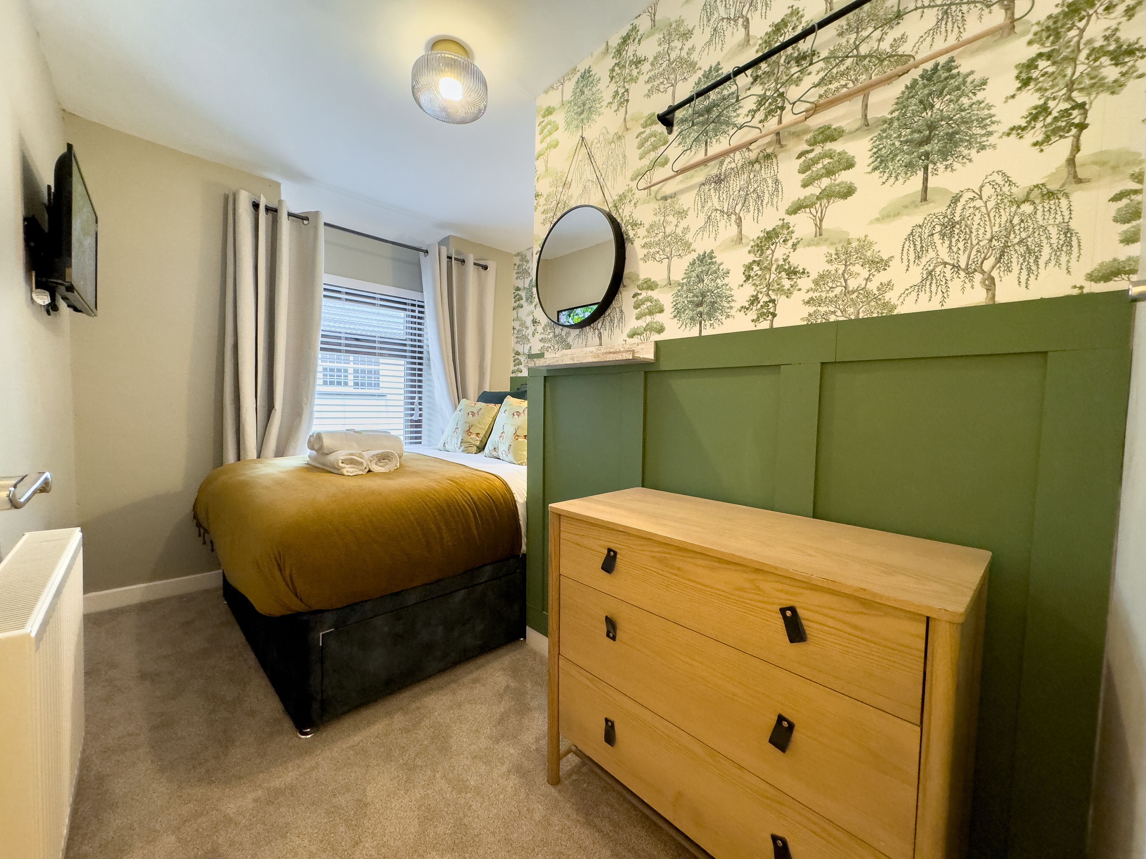 Une chambre à coucher avec un lit, une commode, un miroir et une fenêtre avec des rideaux.
