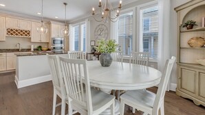 Une cuisine avec des meubles blancs, un îlot central doté de sièges, un lustre et une horloge au mur.