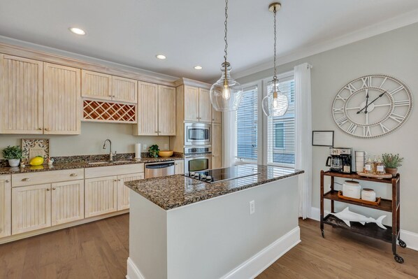 A kitchen with light wooden cabinets, a granite countertop island, stainless steel appliances, and a wall clock. - Hot Tub, Elevator, Game Room, Bikes, 3 blocks to Mid Beach! (Tybee Island)