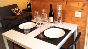 A dining table set with plates, glasses, and a bottle, in a room with wooden walls and a sign that reads "Le plus doux bonheur est l'on partage". - Studio Duplex Avec Terrasse Ombragée (Lempdes)