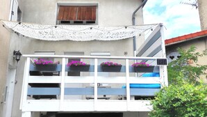 A balcony with white railings, blue cushions, and flower boxes with pink flowers. - Studio Duplex Avec Terrasse Ombragée (Lempdes)