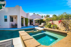 A modern pool area with a clear blue pool, surrounded by a white building with a patio and outdoor seating.