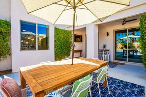 A wooden patio table with chairs, a ceiling fan, and a view of a pool area.