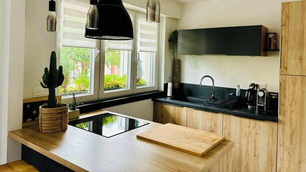 Eine moderne Küche mit schwarzem Arbeitsplatz, Holzschränken, einer schwarzen Rückwand und Pendelleuchten.