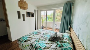 Ein Schlafzimmer mit Bett, einer Hängelampe, einem Balkon mit Stuhl und Blick ins Grüne.