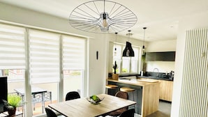 Eine moderne Küche mit Kochinsel, einem Essbereich mit Holztisch und -stühlen sowie einer großen Glastür zum Balkon.