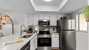 Une cuisine moderne avec des meubles blancs, des appareils en acier inoxydable et un plancher en bois.