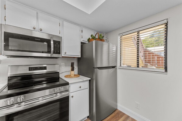 A modern kitchen with stainless steel appliances, white cabinetry, and a window with blinds.