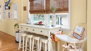 A kitchen with a white countertop, bar stools, a window with blinds, and a child's high chair. - Four Bedroom West OC Home with Pool and Hot Tub (Ocean City)