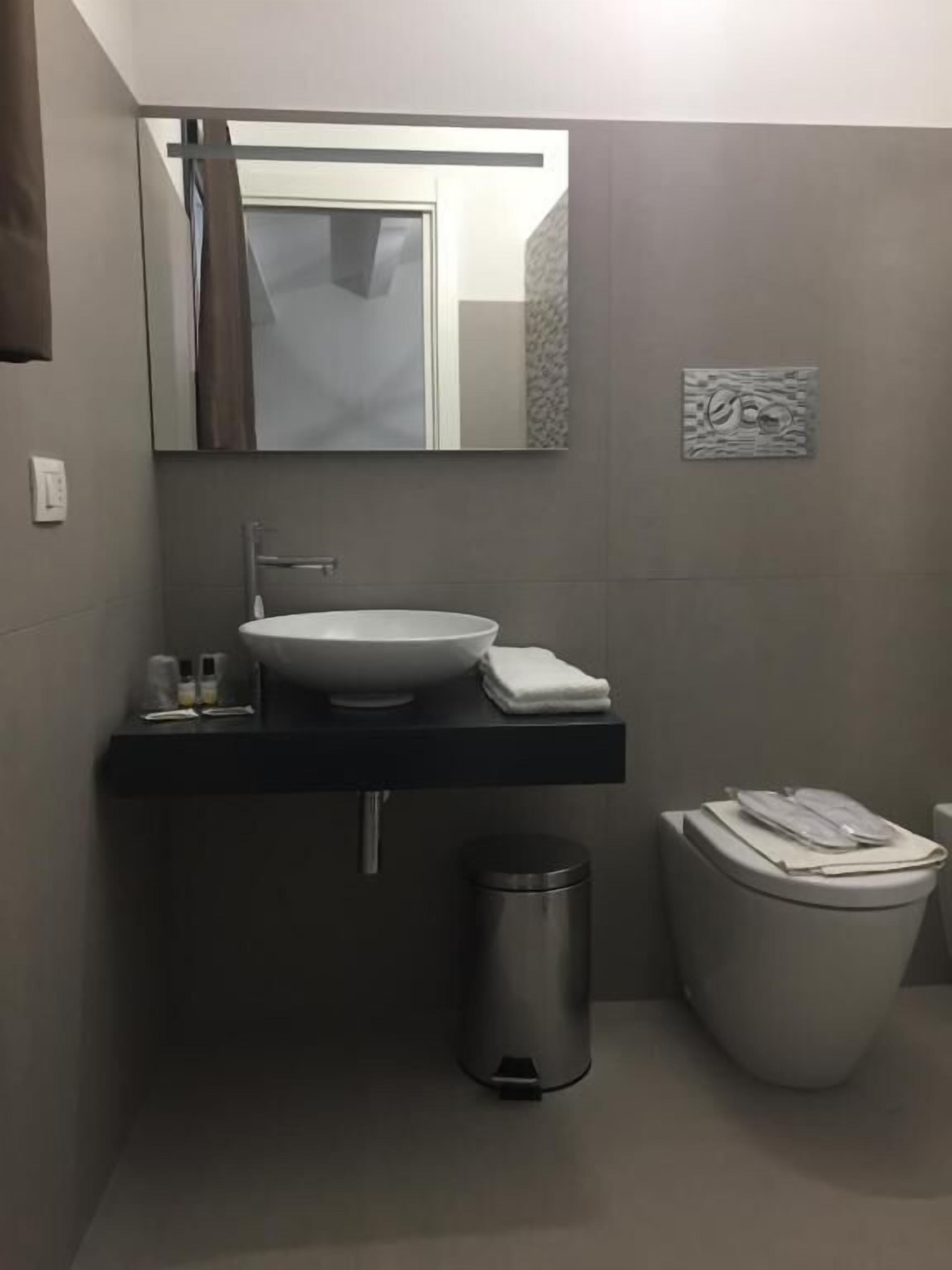 A modern bathroom with a white sink, a mirror, a toilet, and a trash bin.