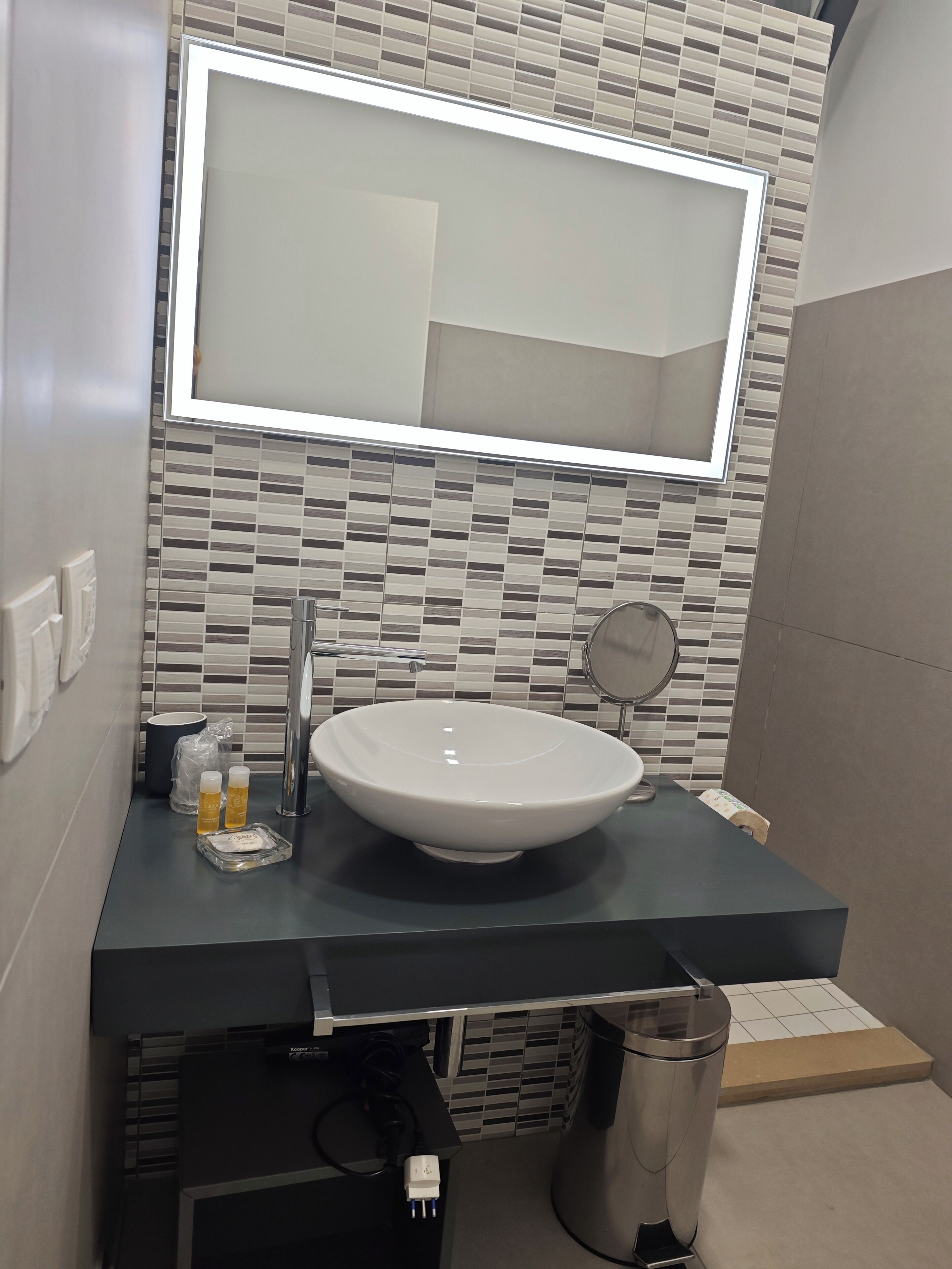 Un baño moderno con un espejo grande, un lavamanos sobremesa y un salpicadero de azulejos.