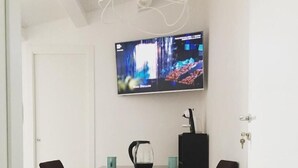 Un comedor moderno con un televisor en la pared mostrando una imagen abstracta y colorida. Hay dos sillas negras y una mesa con una jofaina y una taza.