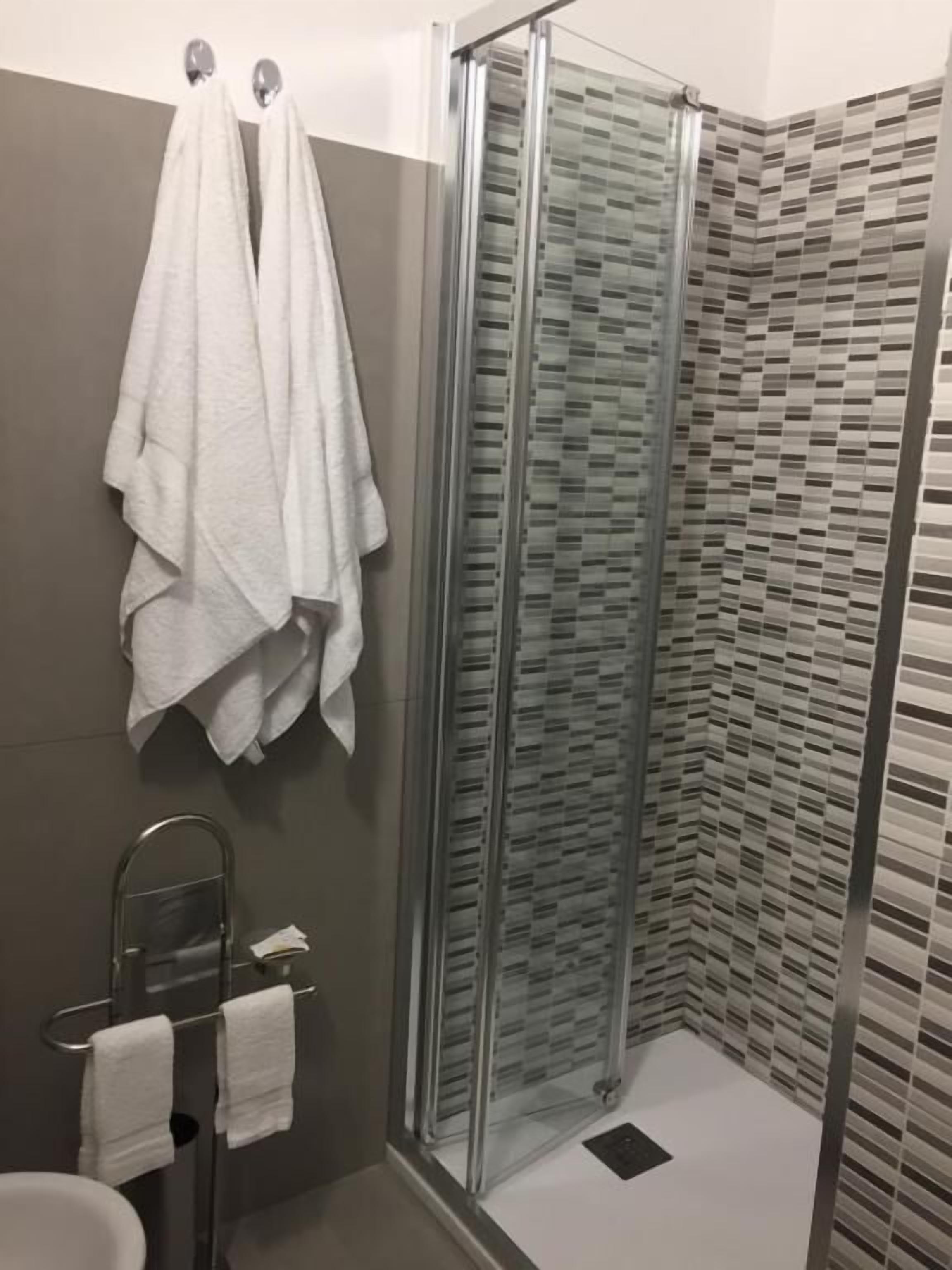 Un baño con cabina de ducha de vidrio, un perchero con dos toallas y una pared con azulejos.