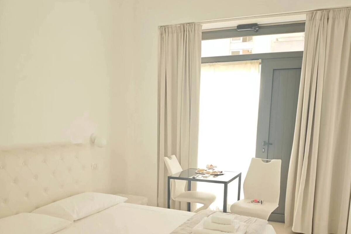 Habitación de hotel con una cama grande, una mesita con una silla y vistas a través de una puerta.