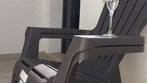Una silla negra de exterior con un vaso de agua encima, sobre un piso de baldosas.