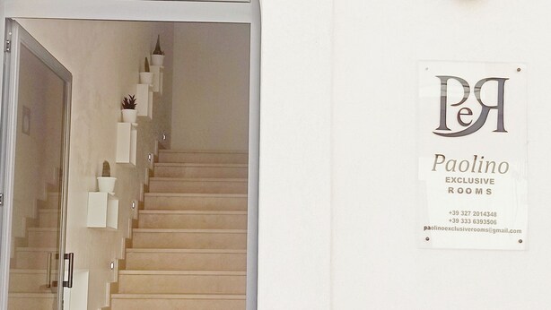Una escalera conduce a una habitación con un letrero que indica 'Paolino Exclusive Rooms'.