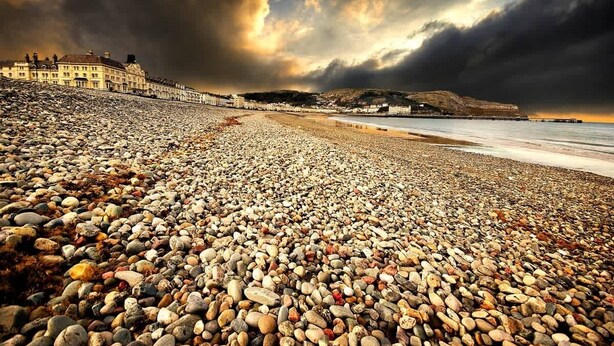A pebbled beach with a row of buildings in the background.