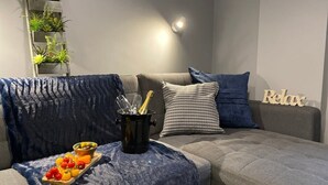A modern living room with a grey sofa, blue cushions, a small plant wall, and a 'Relax' sign.
