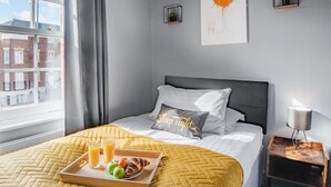 Una cama bien hecha con una bandeja de desayuno, una lámpara de noche y vistas de edificios.