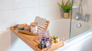 Baño con una bandeja de madera que contiene diversos artículos de aseo, cabina de ducha de vidrio y una planta en maceta.