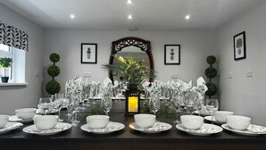 Un comedor con una mesa larga dispuesta para una comida, rodeado de cuadros enmarcados y plantas decorativas.