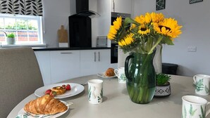 Una mesa de comedor con platos de comida, un croissant y un jarrón de girasoles.