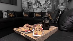 A tray with pastries and a coffee maker on a wooden table in a living room with a black leather couch and pillows with "Relax" text. - Tudor House - Hot Tubs Chester City Sleeps 30 (Cheshire West and Chester)