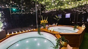 A spa area with two hot tubs, surrounded by wooden benches and potted plants. - Tudor House - Hot Tubs Chester City Sleeps 30 (Cheshire West and Chester)