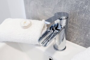 A modern bathroom with a chrome faucet, a white sink, and a towel with a bottle of lotion. - Wrexham Central Stay Apartment Six - Sleeps 5 (Wrexham)
