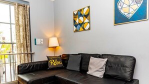A modern living room with a black leather sofa, a table lamp, and abstract art on the walls. - The Berwyn 2 bedroomed Apartment | Central Wrexham (Wrexham)