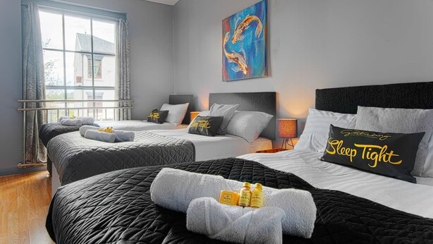 A hotel room with two beds, a large window with curtains, a painting on the wall, and a pillow with "Sleep Tight" text. - The Berwyn 2 bedroomed Apartment | Central Wrexham (Wrexham)
