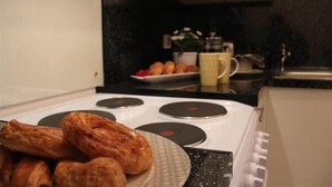 A kitchen with a stove, a plate of pastries, and a counter with a coffee cup and a bowl of fruit. - The Berwyn 2 bedroomed Apartment | Central Wrexham (Wrexham)