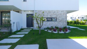 Una casa moderna de dos pisos amb façana de pedra, un arbre petit al jardí i un camí pavimentat que porta a l'entrada.