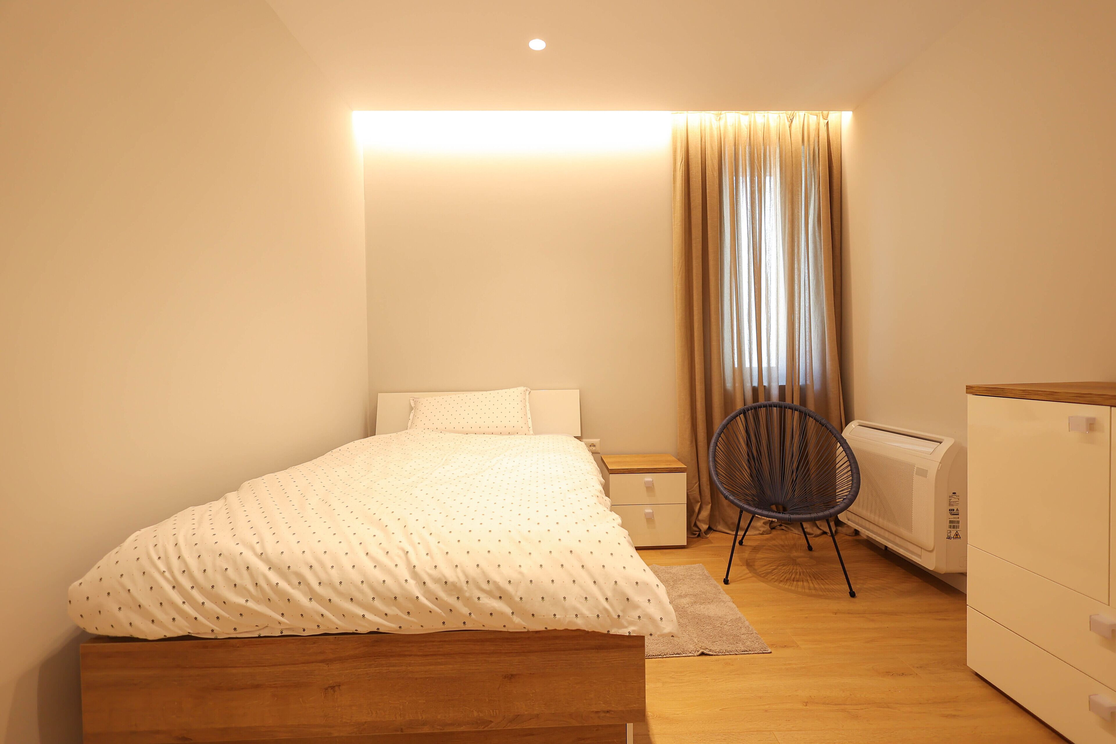 Une chambre à coucher avec un lit en bois, une table de chevet, une chaise, un radiateur et une armoire.