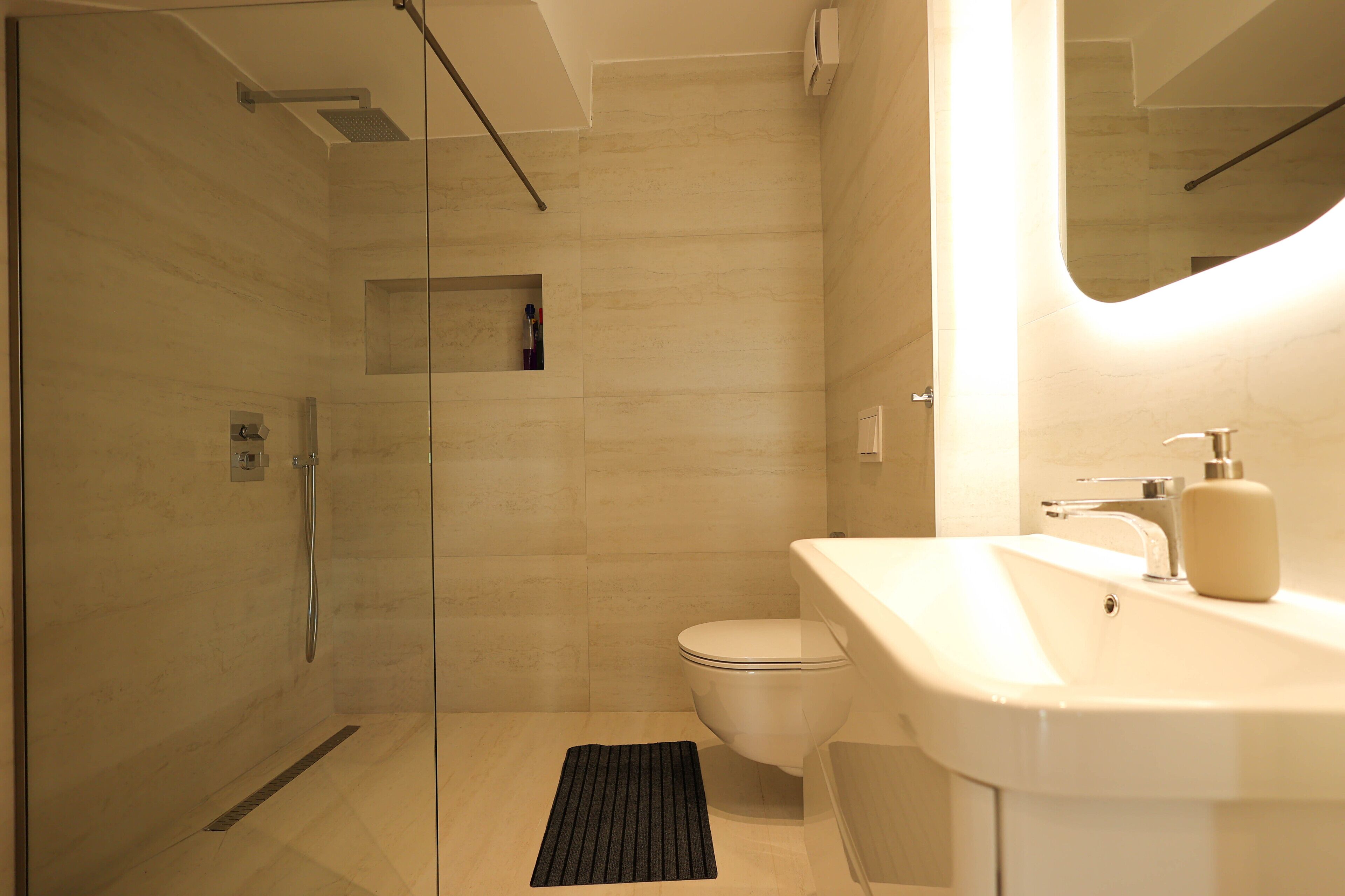 Un baño moderno con ducha envuelta en vidrio, inodoro y lavabo con espejo.