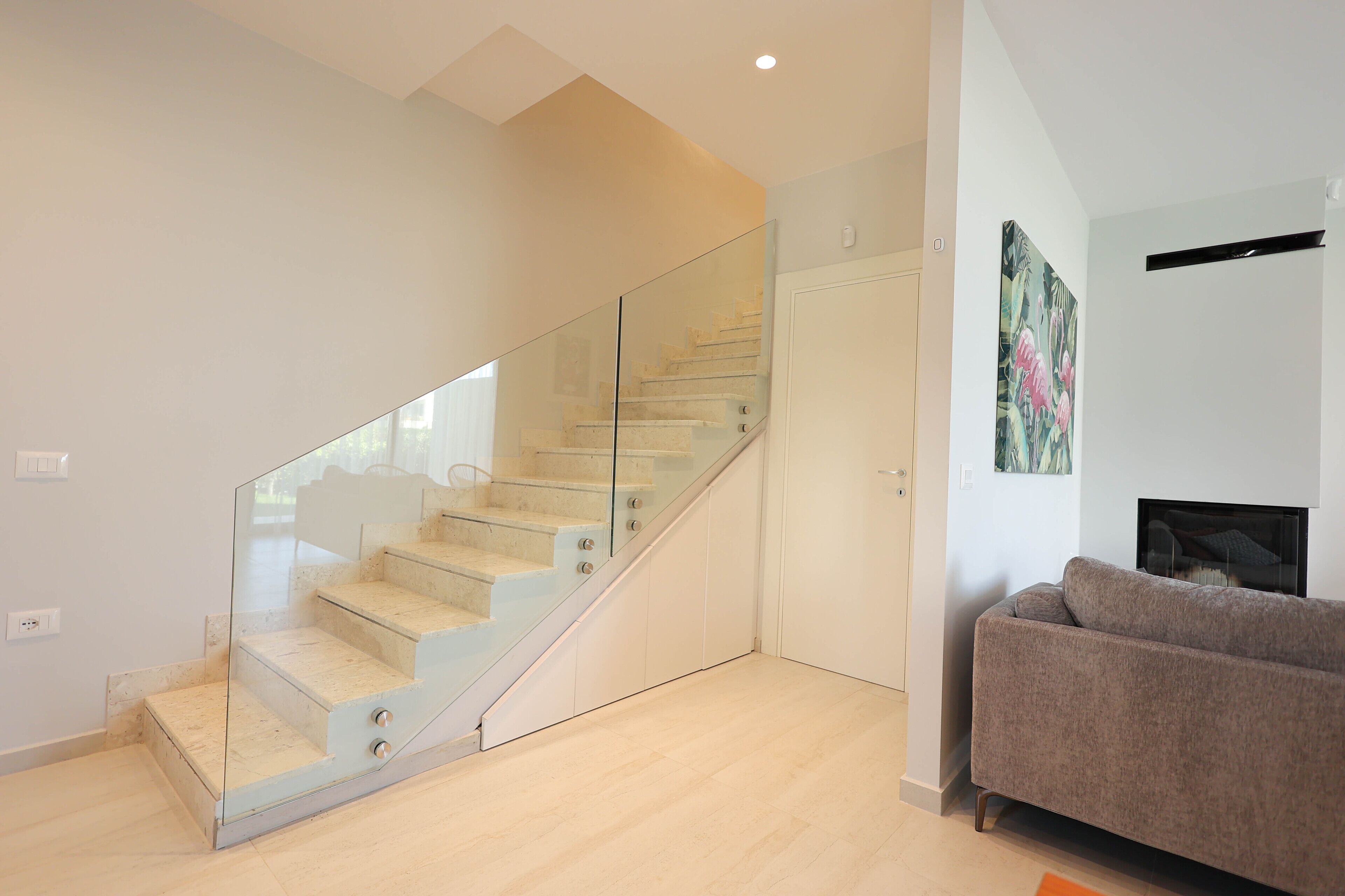 Een modern interieur met een glazen trap, een bank en een schilderij aan de muur.