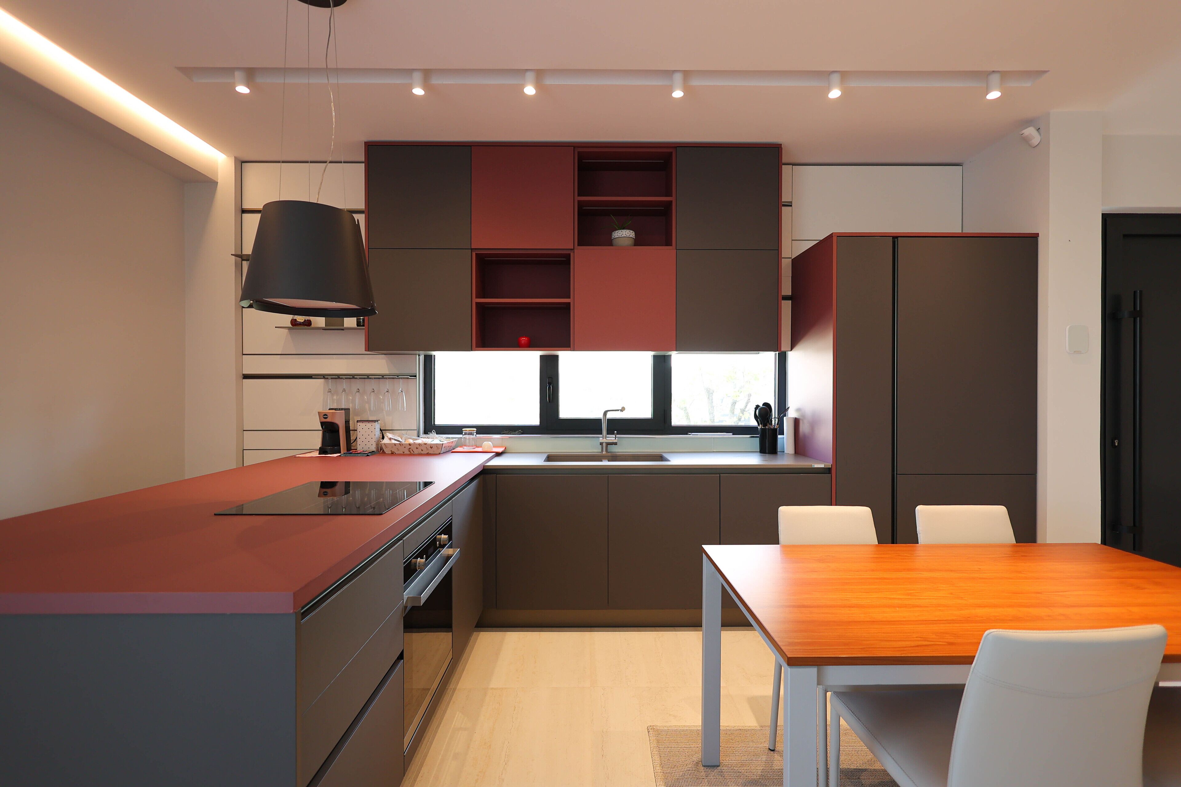 Een moderne keuken met een centraal eiland, inbouwapparatuur en een eetgedeelte met een houten tafel en stoelen.