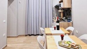 A modern kitchen with white cabinets, a microwave, and a dining area with white chairs and a wooden table. - Miambra (Grumo Nevano)