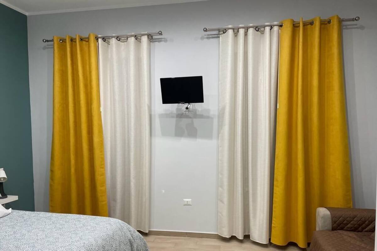 A room with a bed, a desk, a chair, and a TV on the wall.