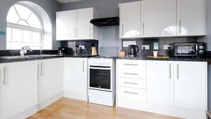 Una cucina moderna con mobili bianchi, forno a incasso, microonde e macchina del caffè.