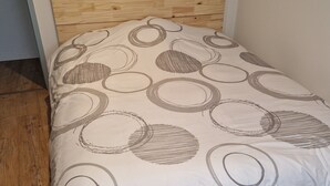 Una cama individual con cabecera de madera y colcha blanca con diseños circulares.