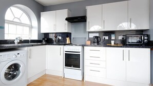 A modern kitchen with white cabinets, a built-in washing machine, a stove, and a microwave. - The Maelor 2 Bedroomed Apartment |Central Wrexham (Wrexham)