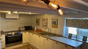 Une cuisine avec des meubles blancs, une cuisinière en acier inoxydable, un évier et une fenêtre agrémentée d’un store à motifs.